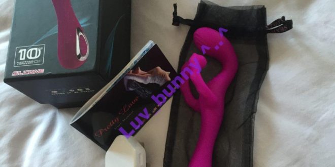 Purple silicone rechargeable G-spot vibrator with fluttery Clitoral stimulator. Displayed with packaging, instruction booklet and charging lead with mains adaptor
