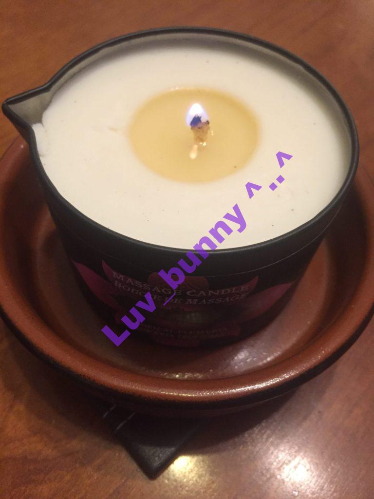 Tropical Plumeria scented massage candle lit and burning in black tin. By Kama Sutra.
