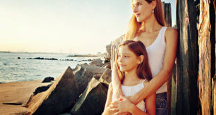 Parenting: Mother & Daughter standing and looking along a beach.