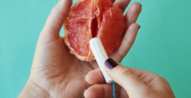 Hands holding a grapefruit segment, with a tampon poised at the front